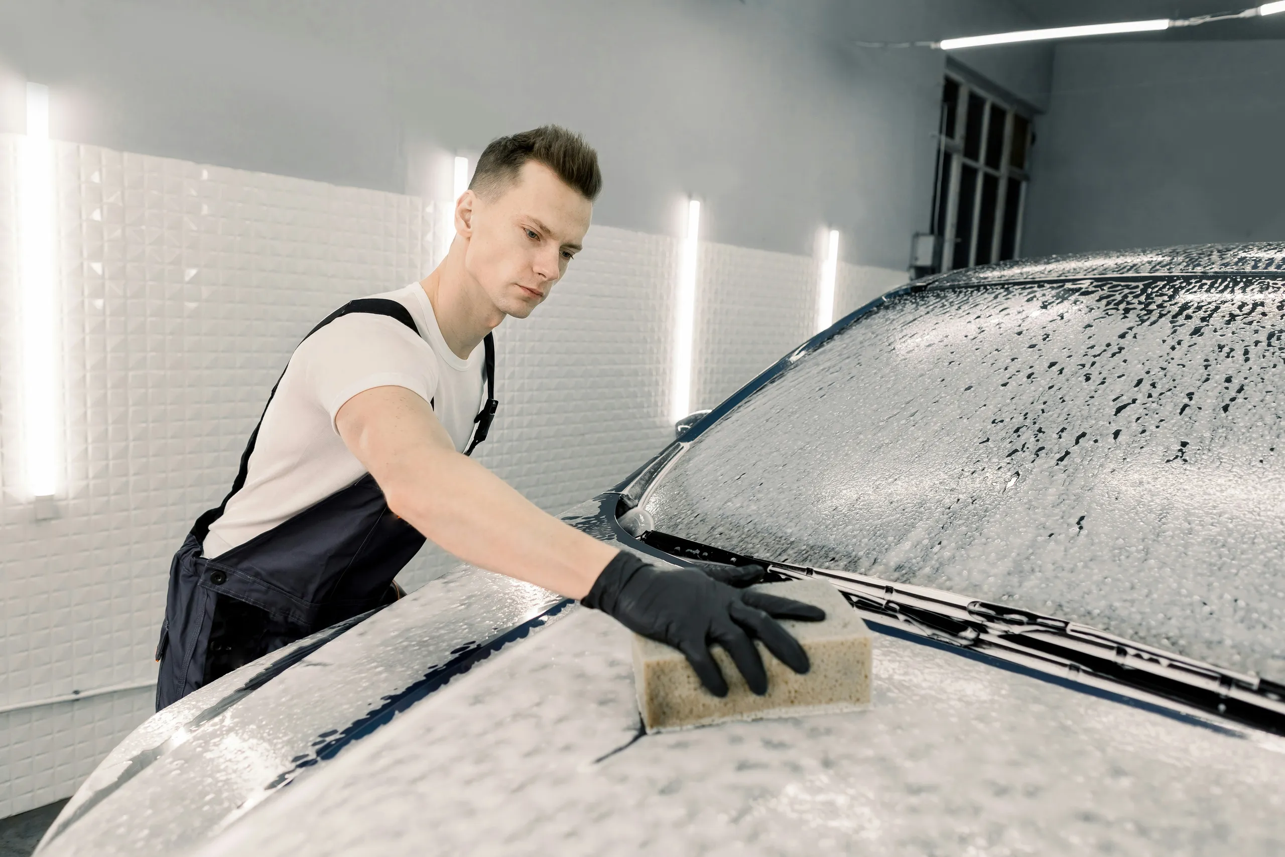 Technik myje gąbką spienioną maskę auta w studio detailingu